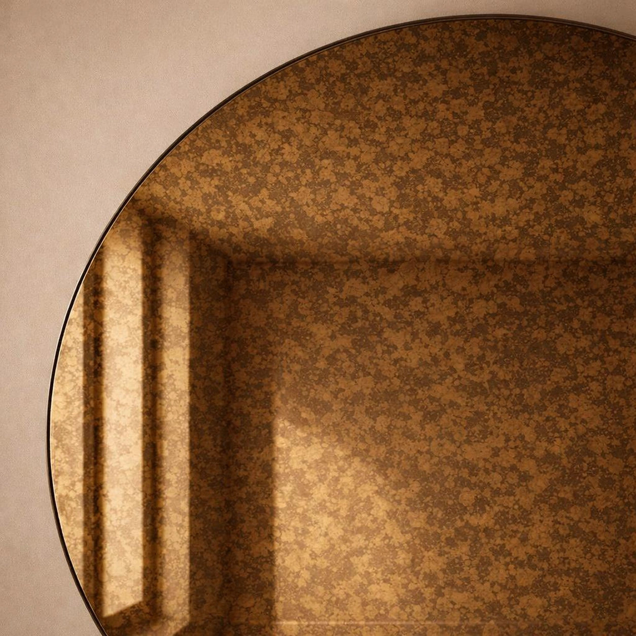 Close-up of an amber cognac antiqued round mirror showing warm foxing and a window reflection