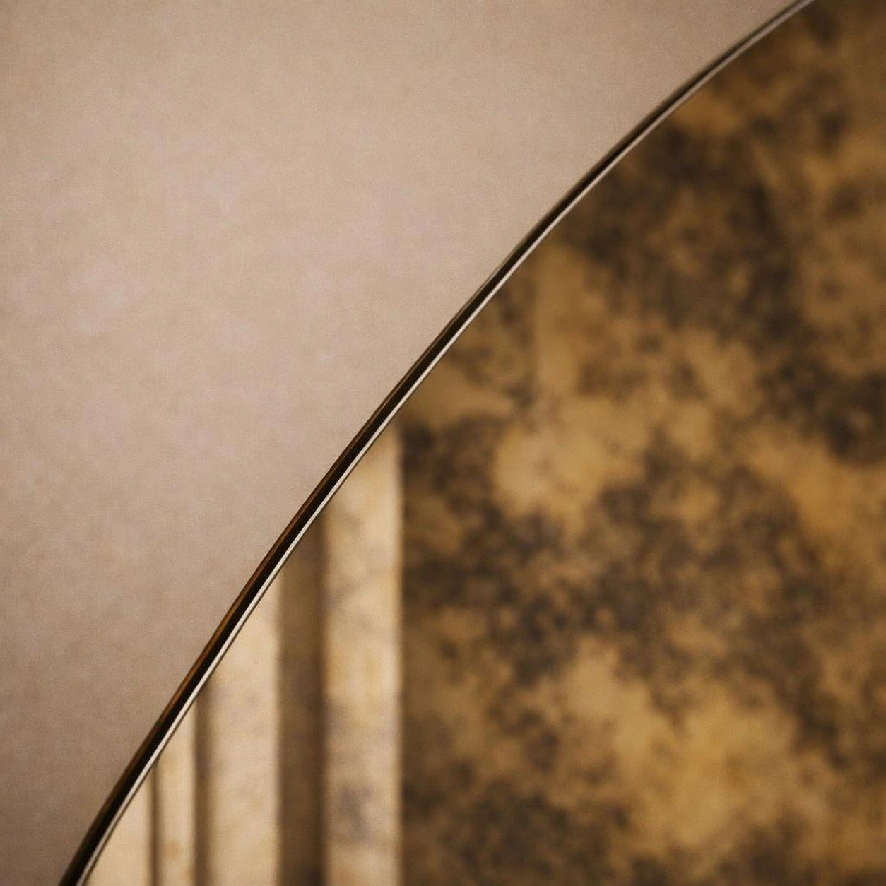 Frameless edge detail of a gold antiqued round mirror with gilded foxing
